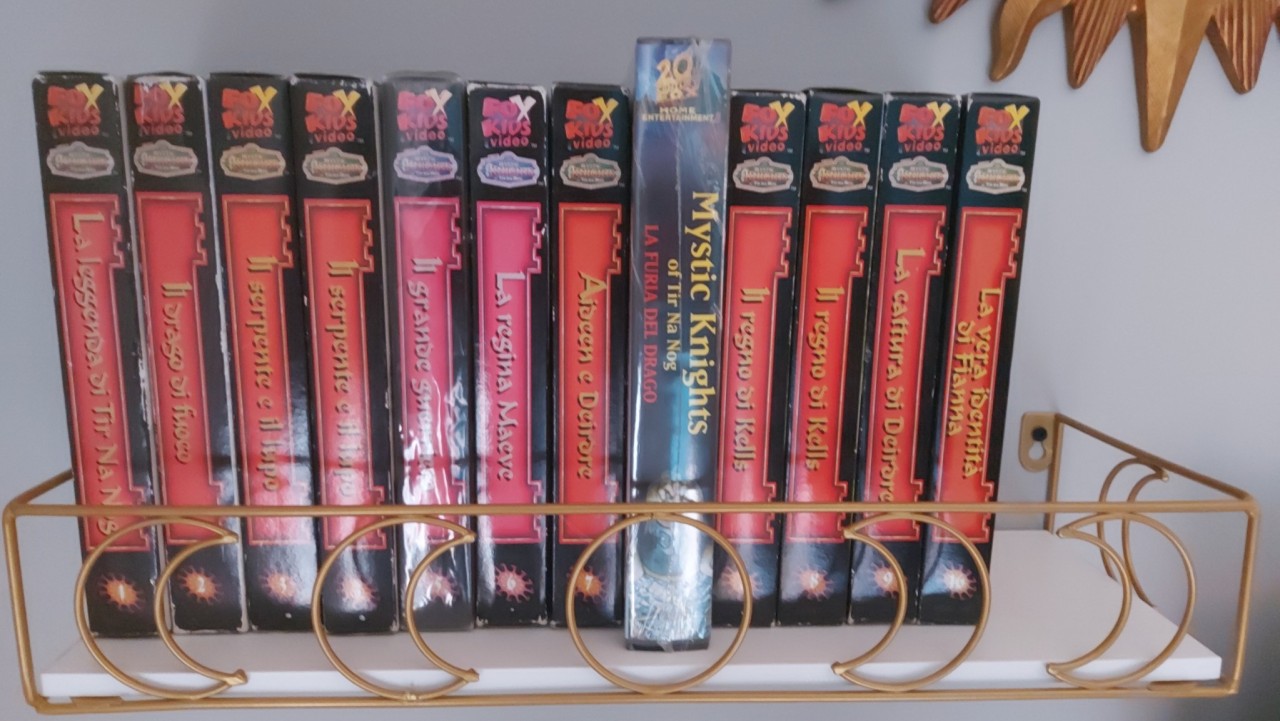 Picture of VHS tapes 1, 2, 3 (twice), 5, 6, 7, the clamshell #2, 8 (twice), 9 and 16 on a shelf. Only the sides are visible, showing the number of each tape. The clamshell #2 tape is is a larger size and in a different style of packaging, making it an obvious standout among the others in the same cardboard sleeve style of packaging.